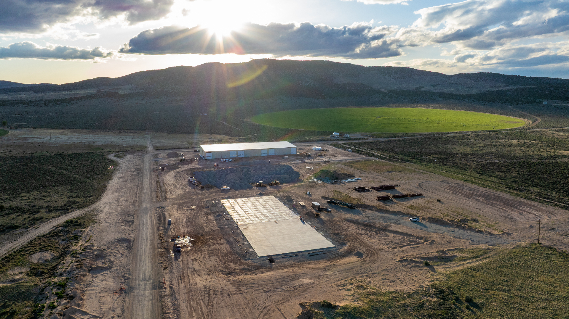 Aerial drone photo of a Southern Utah construction site at golden hour with a freshly poured concrete pad, stockpiles, and equipment staged for the next milestone