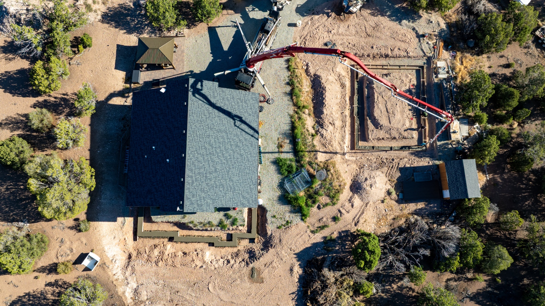 Overhead drone view of a concrete pump pouring a foundation next to a completed structure