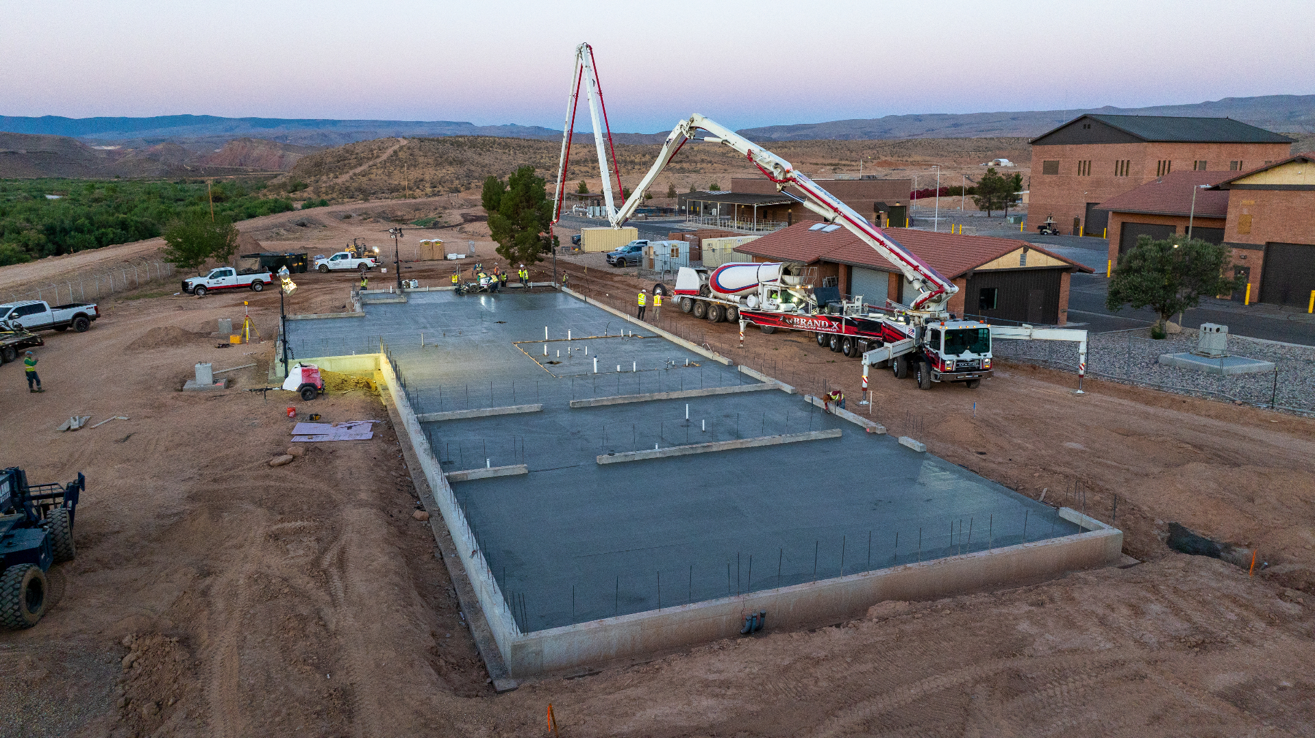 Aerial drone view of a concrete pump truck pouring the foundation slab for the St. George Pre-Treatment Plant addition in Bloomington, Utah at dusk