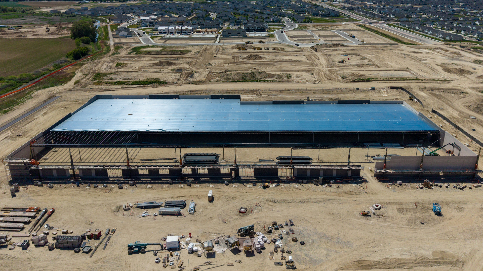 Aerial view of a large commercial building under construction with surrounding earthwork and staged materials