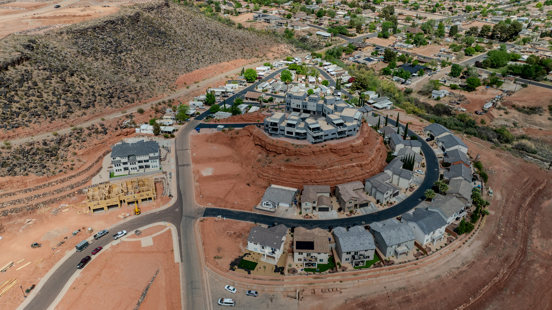 Aerial drone view of a hillside residential development built on a red rock mesa in Southern Utah, with framing under construction nearby