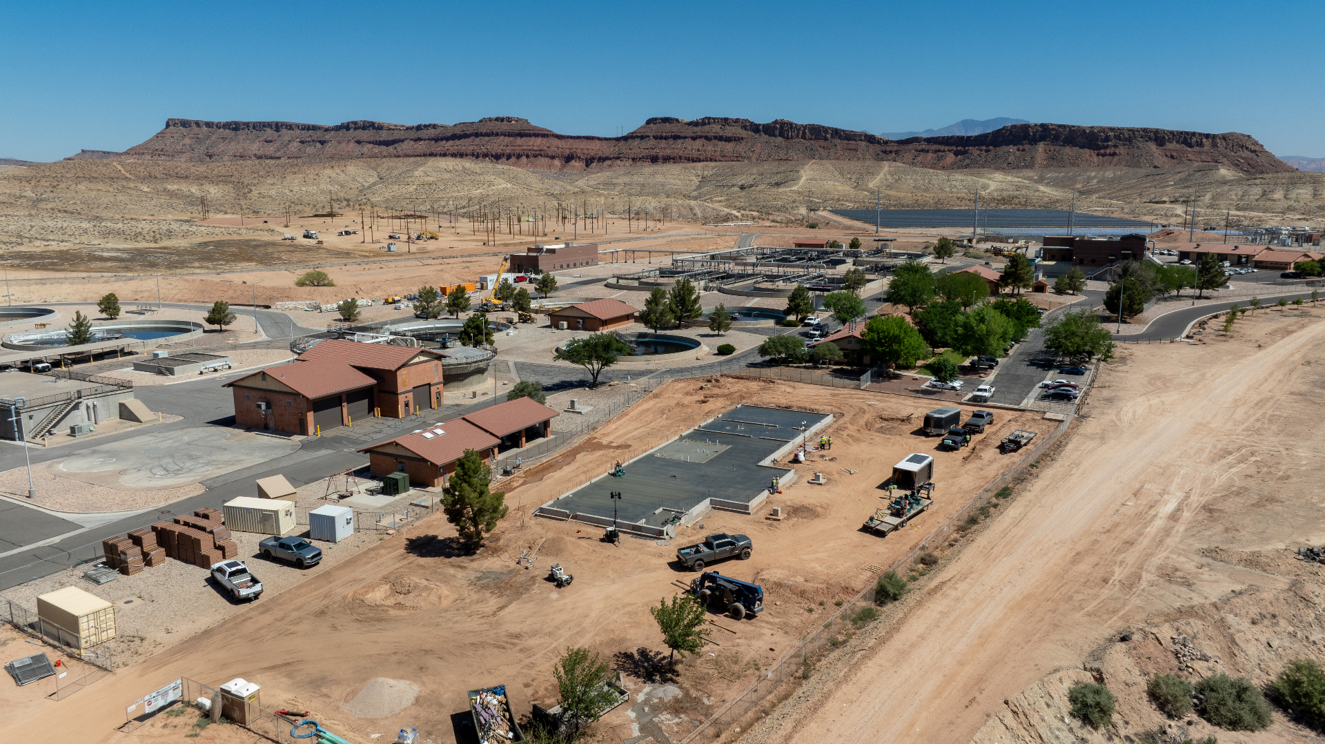 Aerial drone view of a freshly poured concrete pad at the St. George Pre-Treatment Plant addition in Bloomington, Utah, with the existing facility and red rock mesas in the background